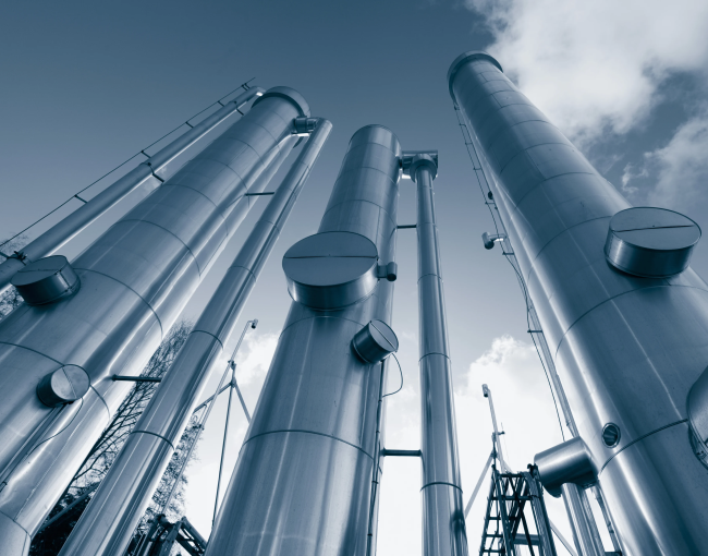 Blue-toned industrial scene looking upward at tall large-diameter stainless steel columns and vessels against cloudy sky