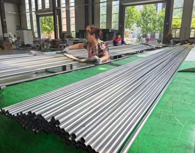 Female factory worker sorting and inspecting polished stainless steel round tubes on production line in Chinese factory