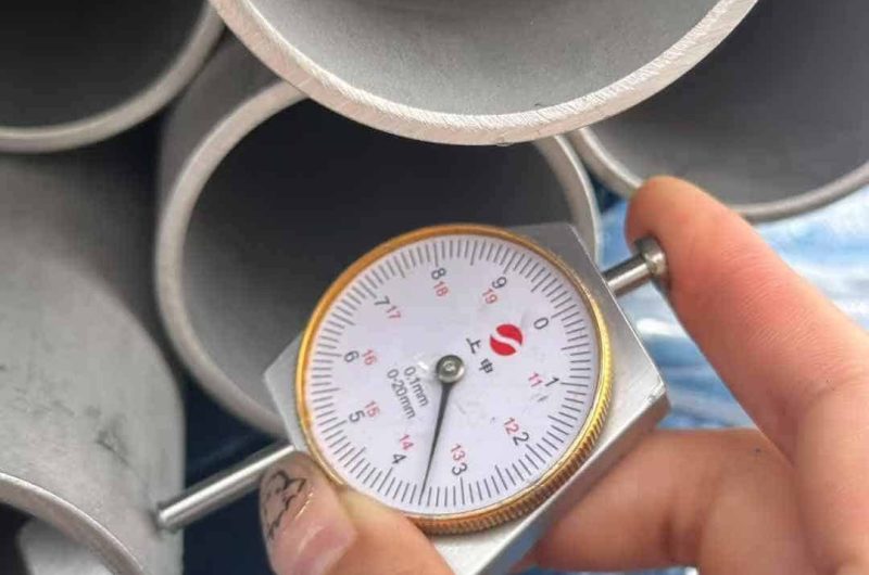 A person holding a measuring device next to a stack of pipes.